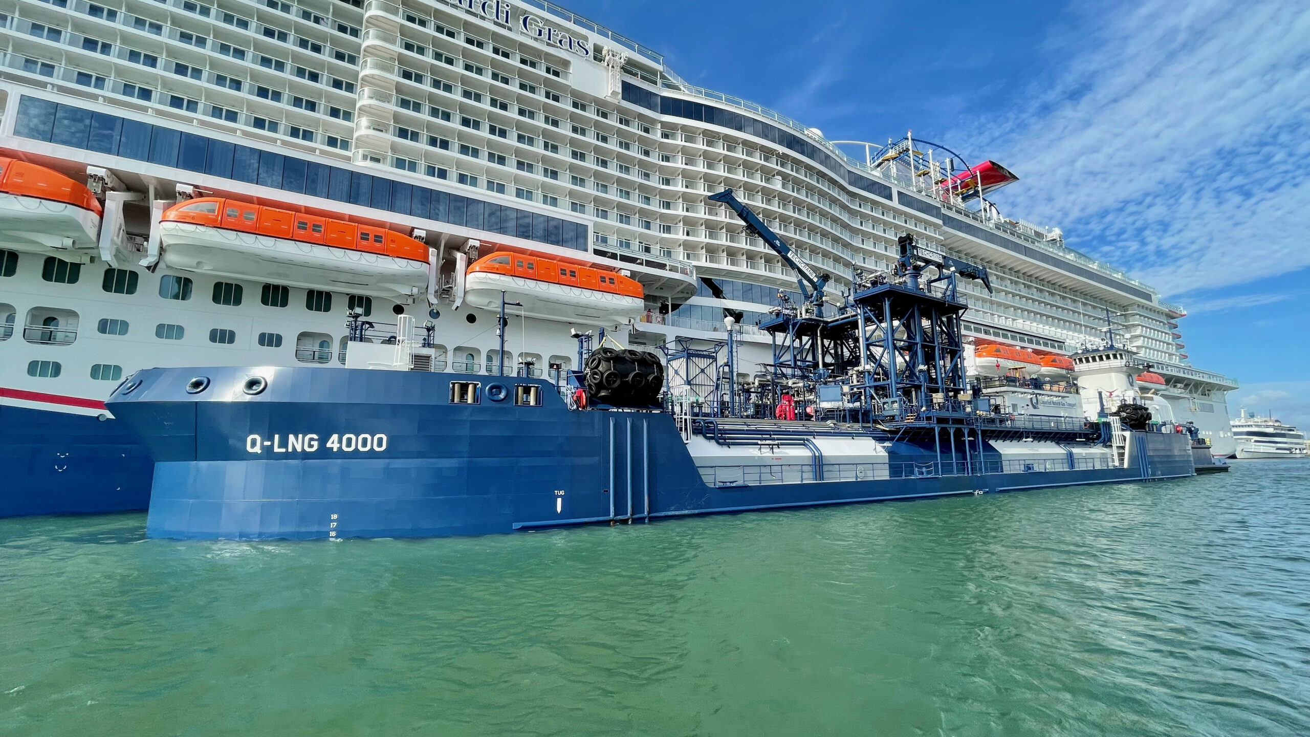 Q-LNG 4000 refuels the Mardi Gras cruise ship with LNG, showcasing sustainable maritime practices under clear skies.